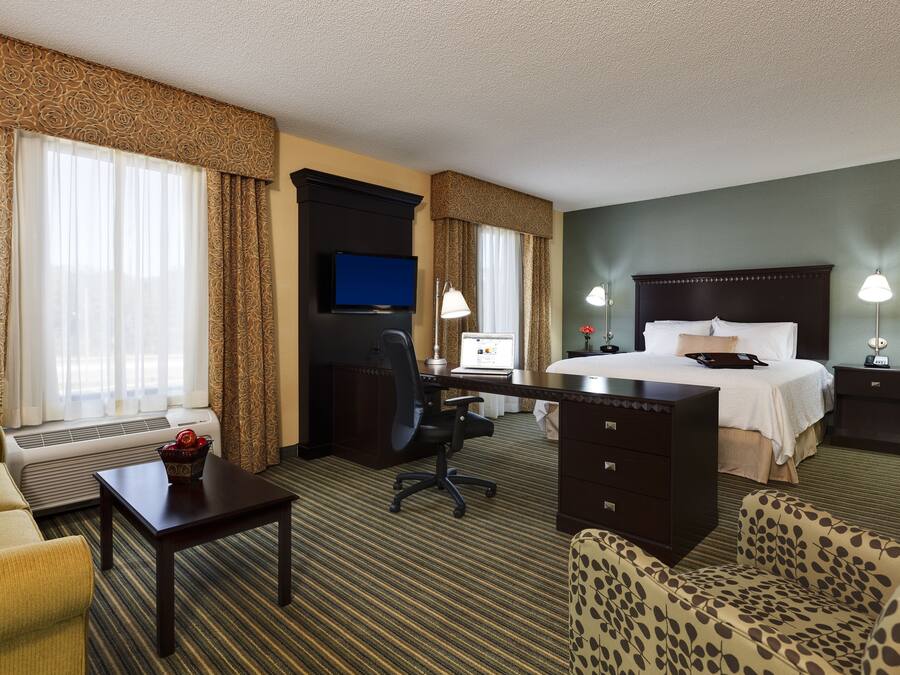 A hotel room with a bed, desk, computer, and two chairs.