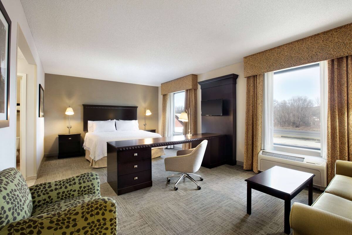 A hotel room with a bed, desk, chair, and TV.