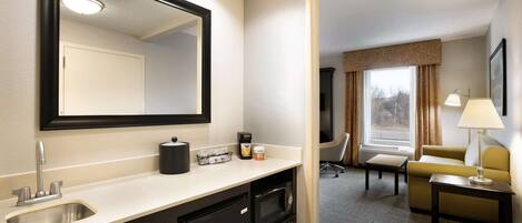 Habitación de hotel con kitchenette, un espejo grande, sofá y ventana con cortinas.