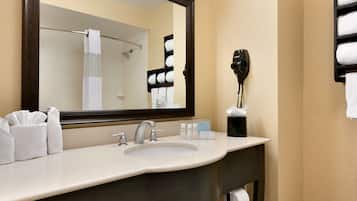 A hotel bathroom with a large mirror, a sink, a hairdryer, and a towel rack.
