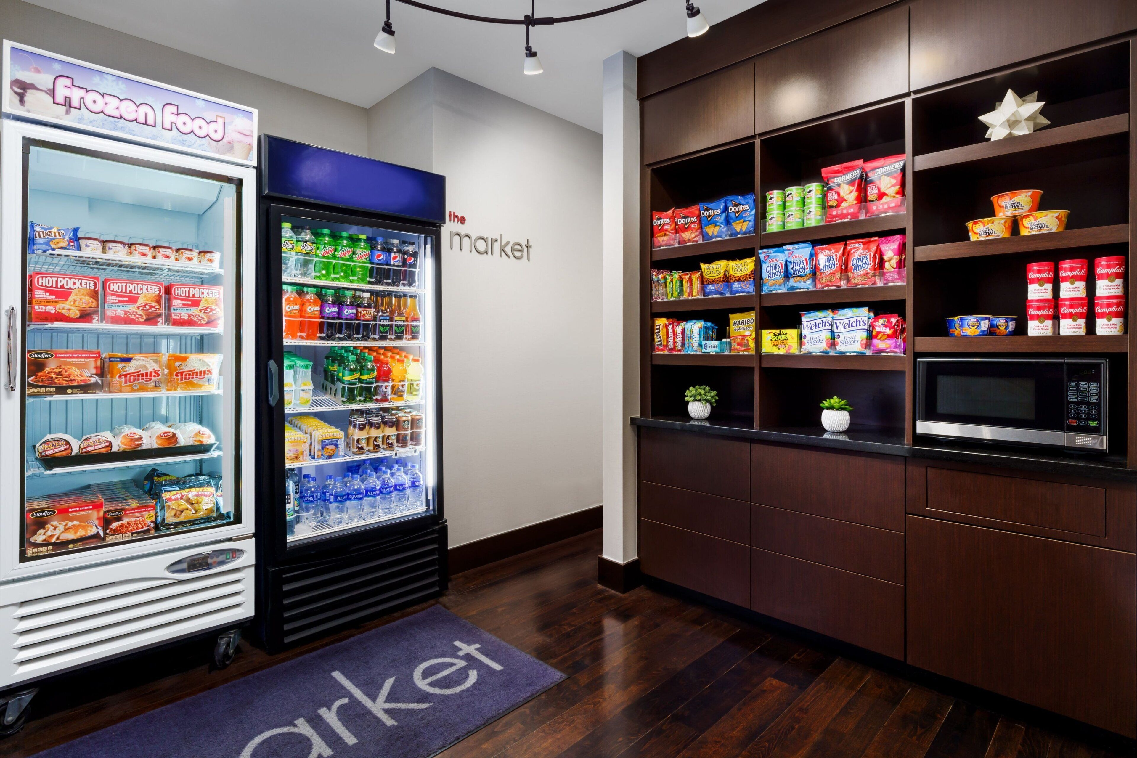 A frozen food section with a freezer and a refrigerator, a microwave, and shelves stocked with snacks and beverages.