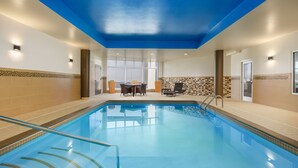 An indoor swimming pool with clear water, a glass railing, and a seating area with tables and chairs. - Courtyard by Marriott Keene Downtown (Keene)