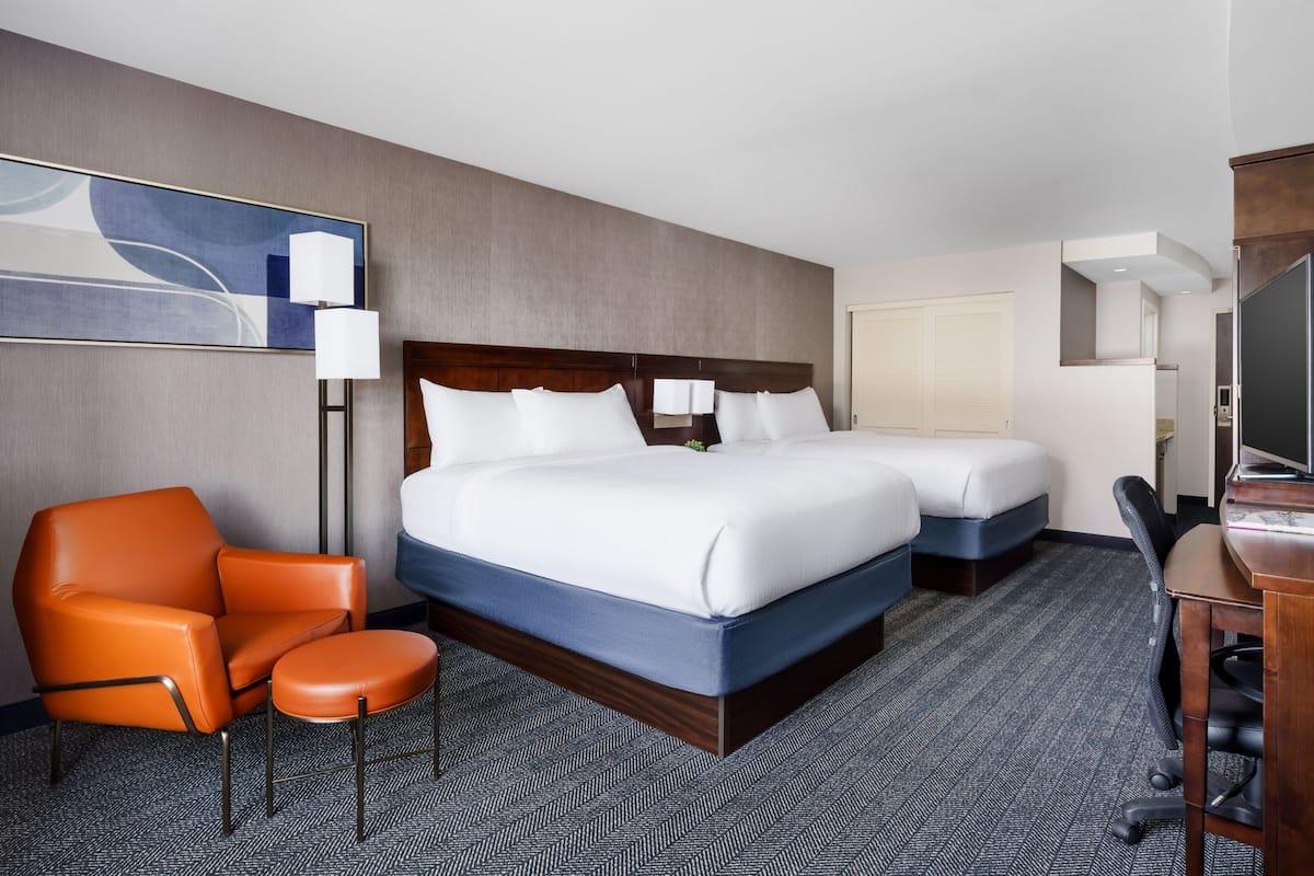 A hotel room with a large bed, a smaller bed, a desk, a chair, and a large painting on the wall.