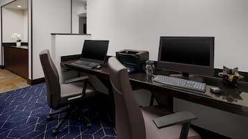 Un espacio de oficina moderno con dos escritorios, cada uno con una computadora portátil y un monitor de escritorio. Hay dos sillas, una impresora y un teclado en los escritorios.