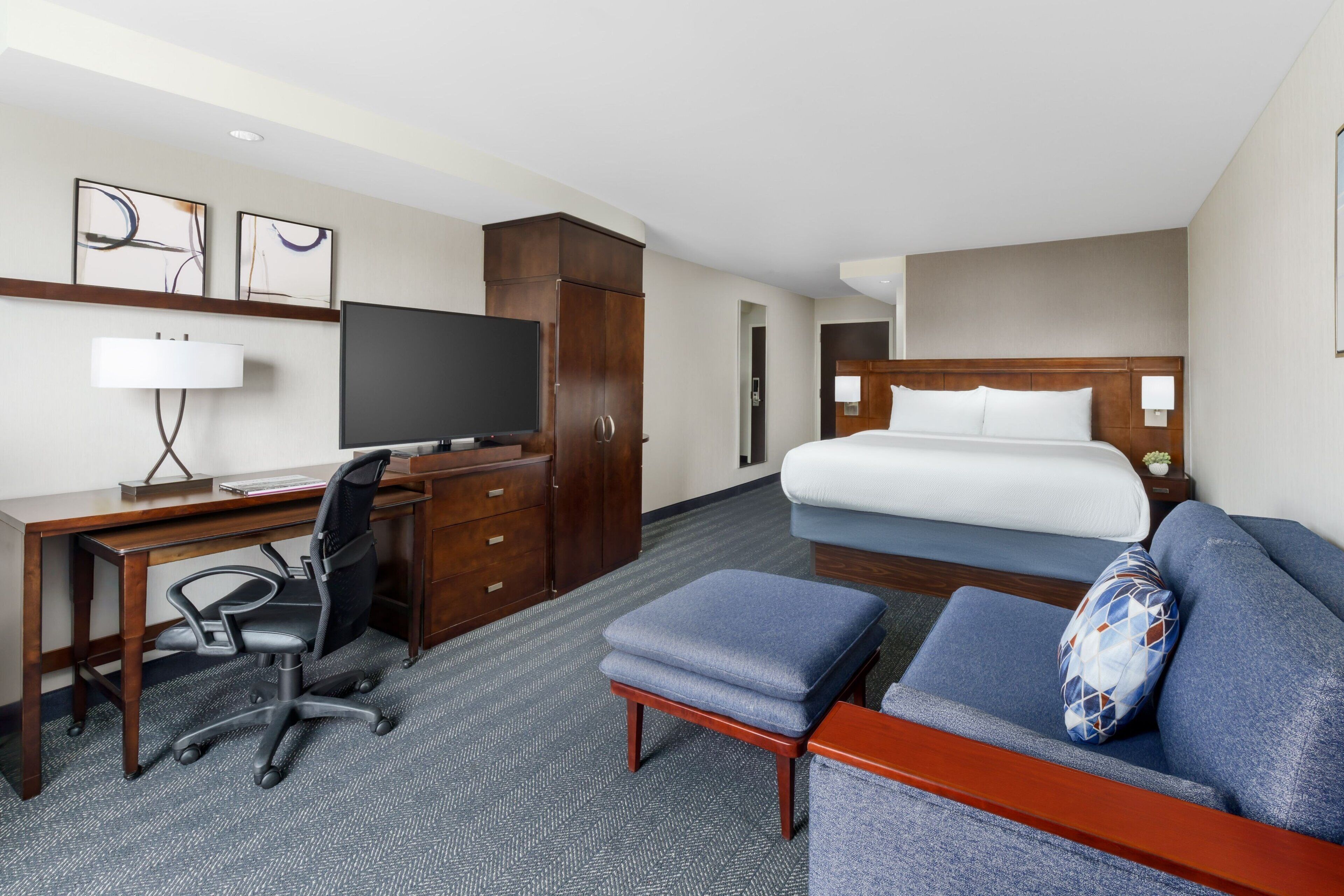 A hotel room with a bed, a desk with a computer, a chair, a TV, and a sofa.