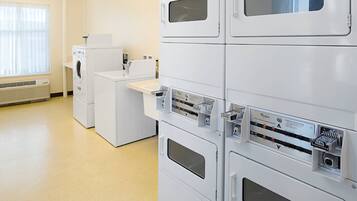 A laundry facility with stacked washing machines and dryers, a countertop with a sink, and a window with blinds.