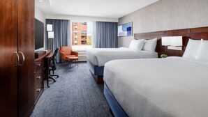 A hotel room with two beds, a desk, an orange chair, and a view of buildings through the window. - Courtyard by Marriott Keene Downtown (Keene)