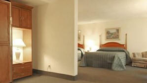 A hotel room with a bed, a nightstand with a lamp, a wooden wardrobe, and a painting on the wall. - River Terrace Green River (Green River)
