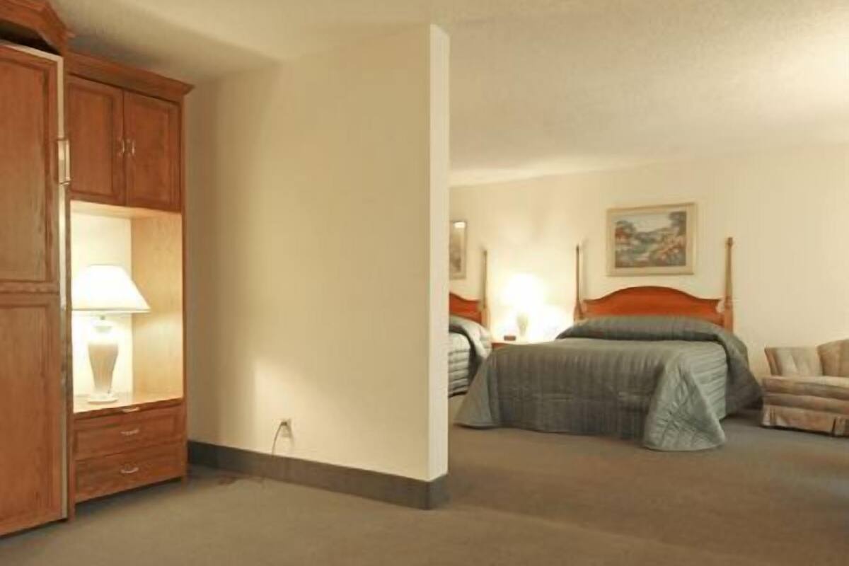 A hotel room with a bed, a nightstand with a lamp, a wooden wardrobe, and a painting on the wall.