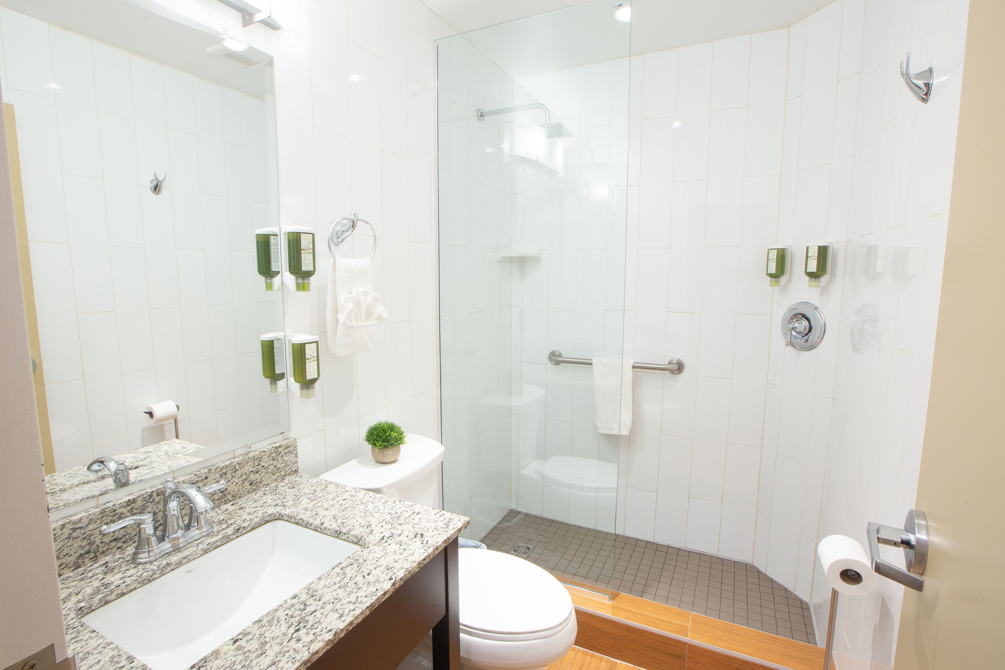 A modern bathroom with a granite countertop sink, a toilet, and a glass-enclosed shower.
