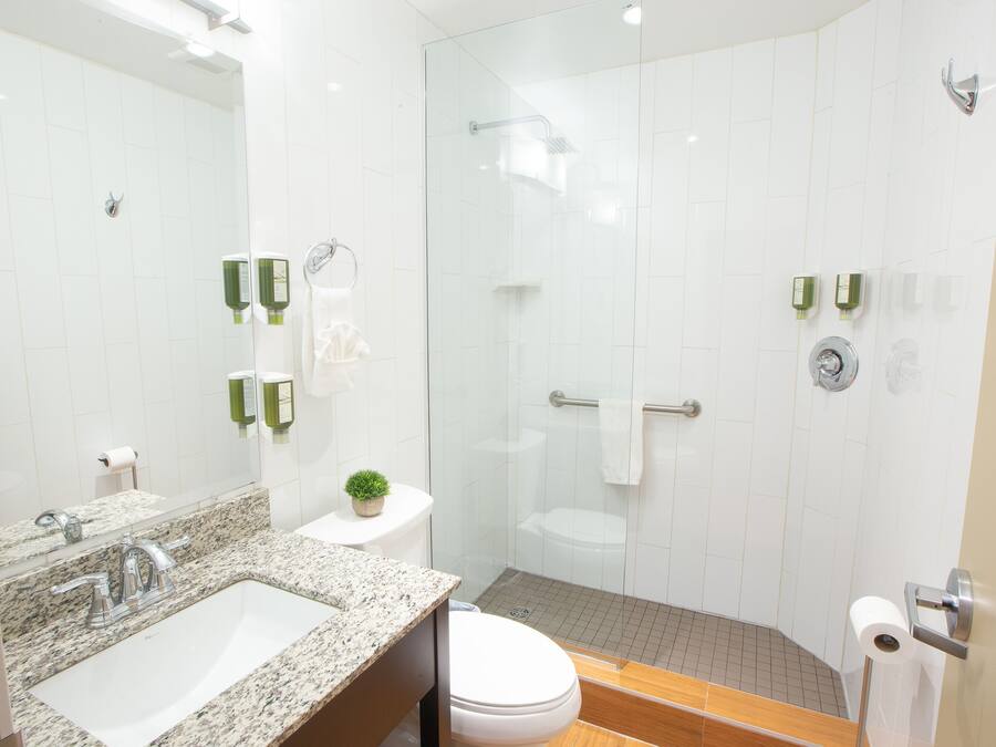 A modern bathroom with a granite countertop sink, a toilet, and a glass-enclosed shower.