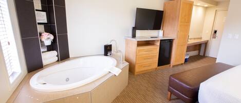 A modern hotel room with a large bathtub, a flat-screen TV, a wooden cabinet, and a bed.