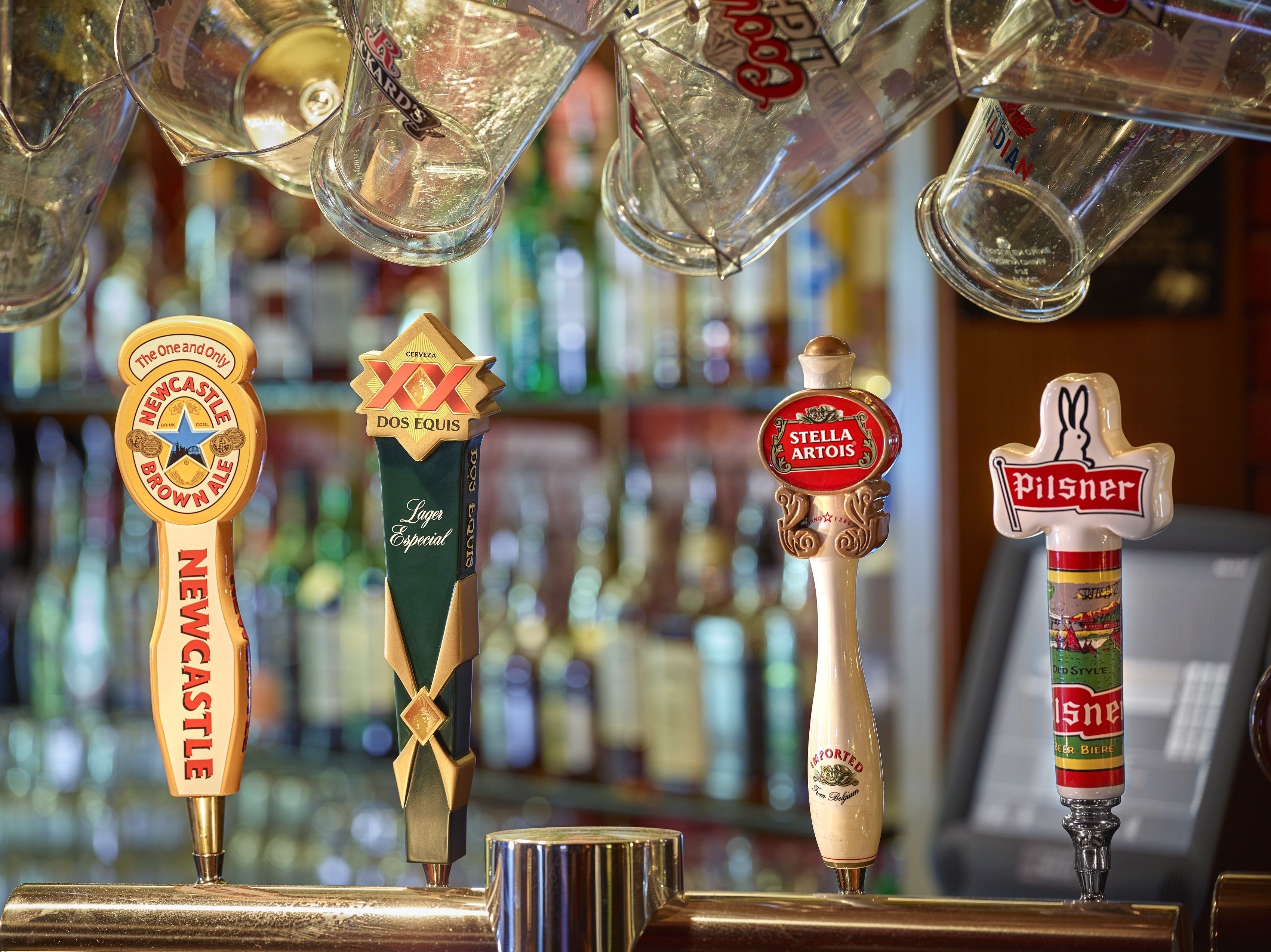 Un bar con diferentes grifos de cerveza, incluyendo Newcastle Brown Ale, Dos Equis, Stella Artois y Pilsner.