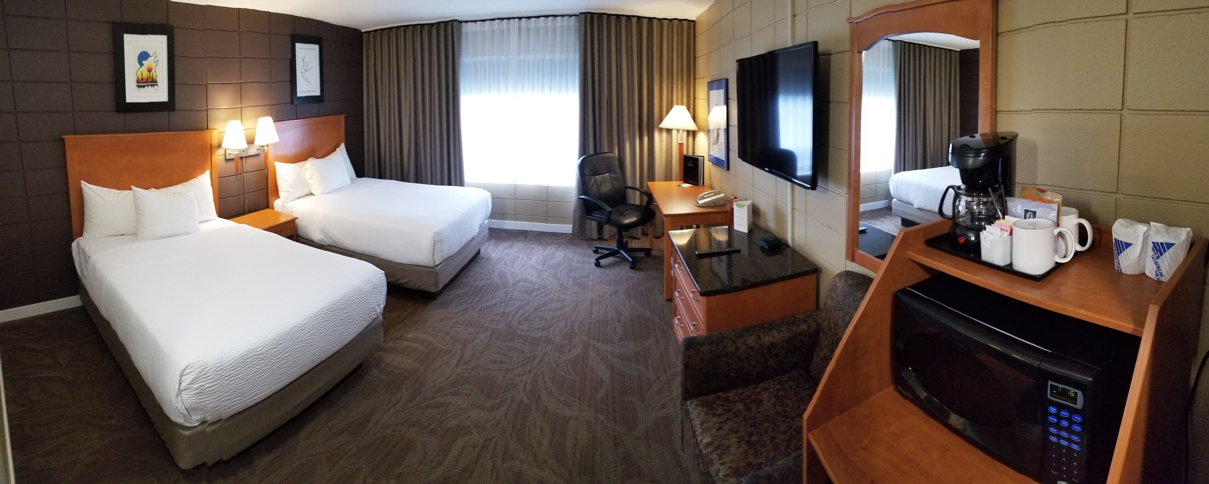 A hotel room with two beds, a desk with a chair, a television, a coffee maker, and a microwave.