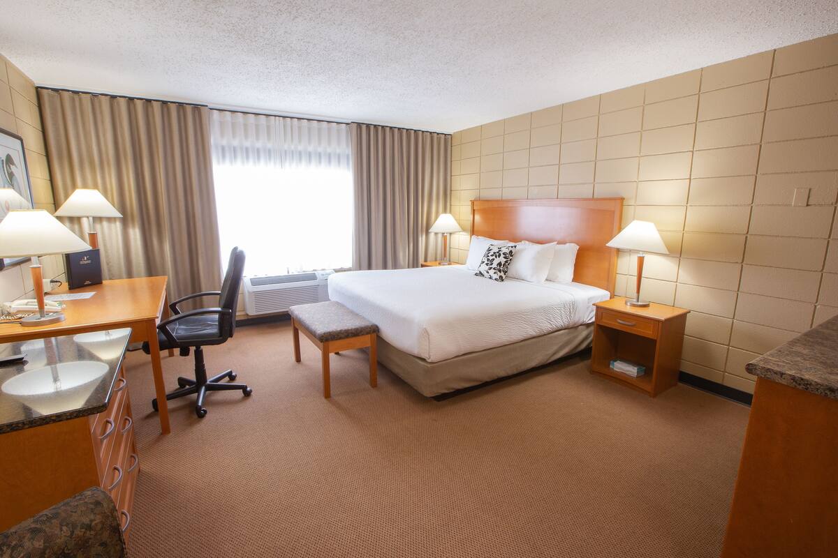A hotel room with a bed, desk, chair, and two bedside tables with lamps.