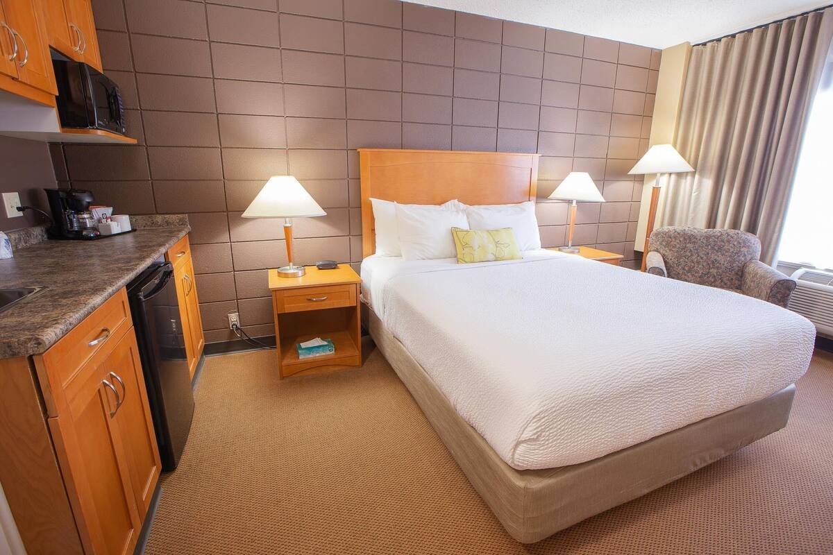 A hotel room with a large bed, two bedside tables with lamps, a chair, a small table with a coffee maker, and a microwave on the countertop.