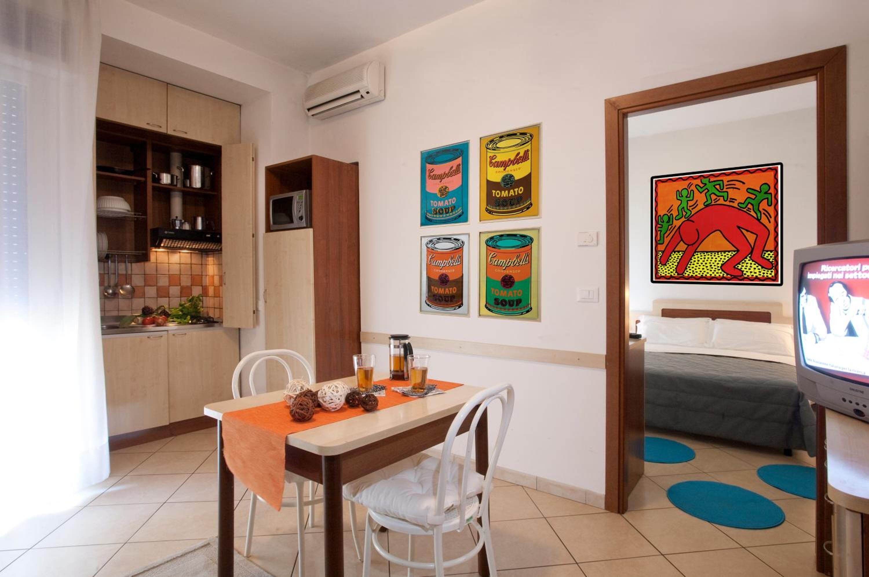 A compact kitchen with a dining area, a bed, and a TV.