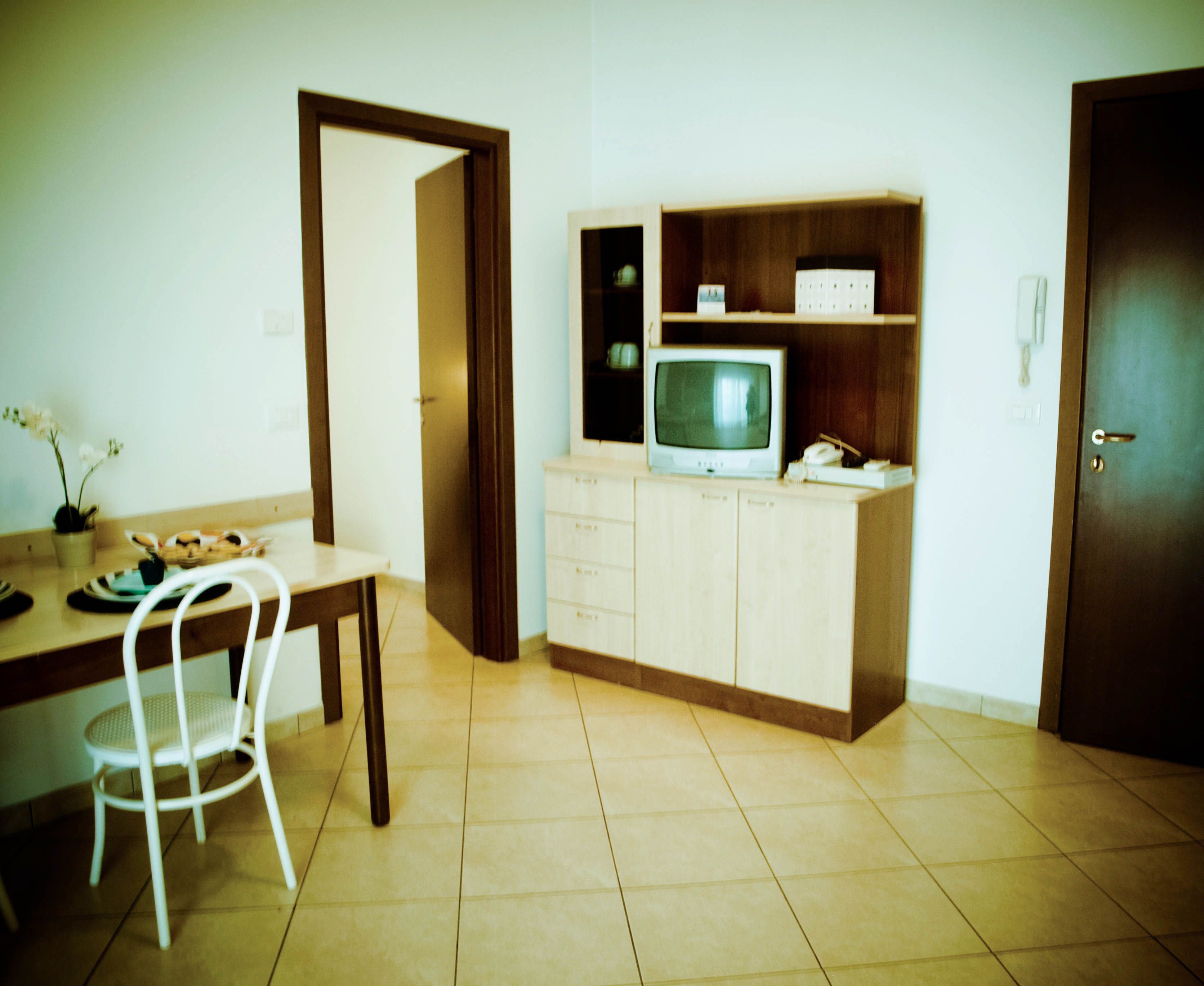 Ein Zimmer mit Esstisch, Stühlen, einem Fernseher auf einem Schrank und einer Tür.