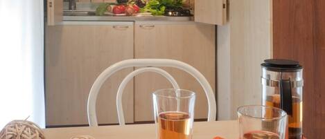A kitchen with wooden cabinets, a microwave, and a sink. There are two chairs and a table with two glasses of tea.
