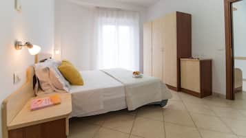 A hotel room with a bed, bedside table, lamp, wardrobe, and a window with curtains.