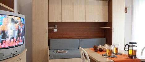 A compact living space with a sofa, a dining table, a coffee maker, and a television.