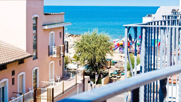 A coastal building with a balcony overlooking a beach with umbrellas and a playground. - Residence Mediterraneo (Rimini)