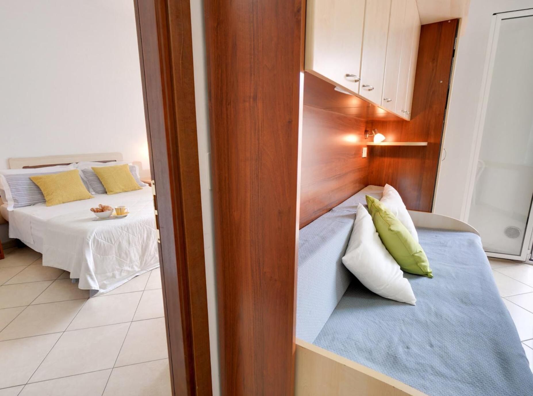 A hotel room with two beds, a wooden headboard, and a small kitchenette.