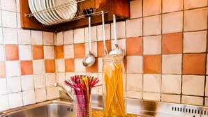 A kitchen with a tiled backsplash, a stainless steel sink, a woven placemat, a jar of spaghetti, and a pot on the stove. - Residence Mediterraneo (Rimini)