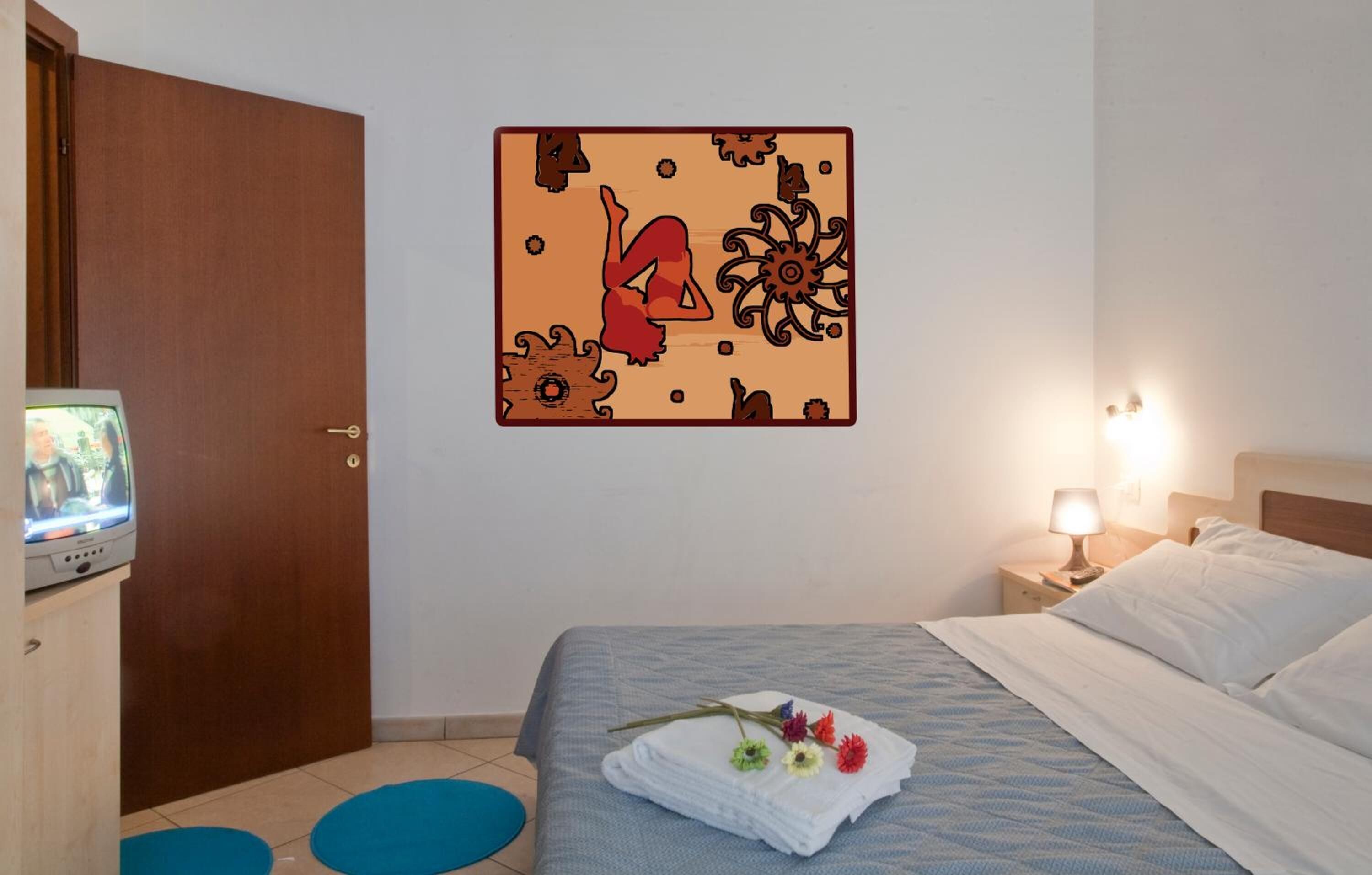 A hotel room with a bed, a wall decoration, a television, and a nightstand with a lamp.