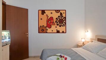 A hotel room with a bed, a wall decoration, a television, and a nightstand with a lamp.