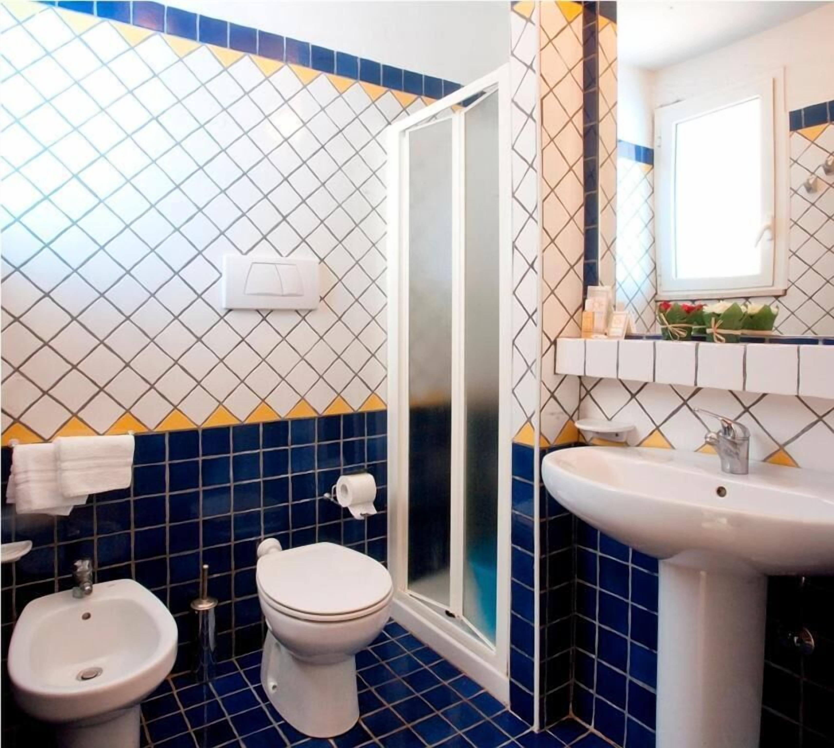 A bathroom with a toilet, bidet, and sink, featuring blue and white patterned tiles.