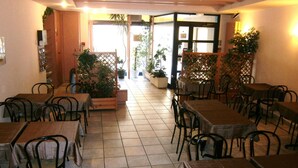 Un restaurant doté de nombreuses tables et chaises, de plantes en pot et d’un sol carrelé.
