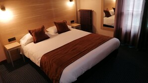 Une chambre d’hôtel avec un grand lit, deux tables de chevet, un miroir et un radiateur.