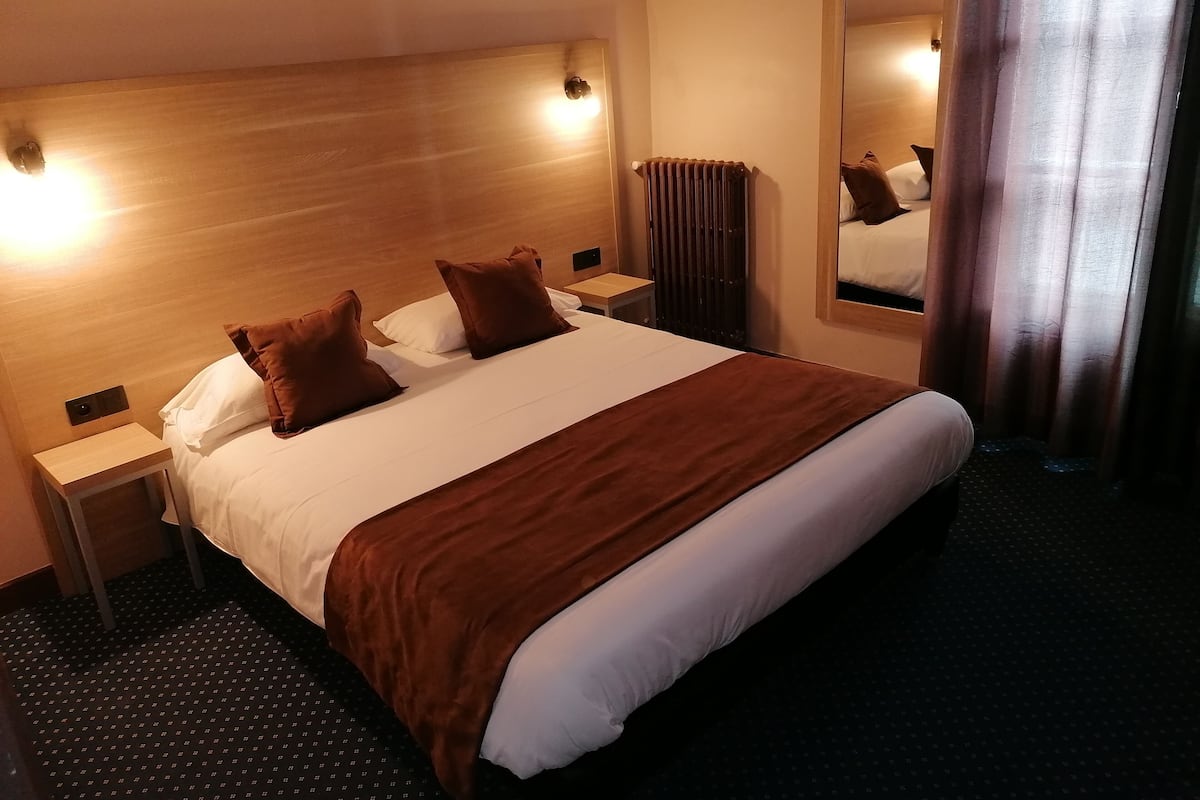 A hotel room with a large bed, two nightstands, a mirror, and a radiator.