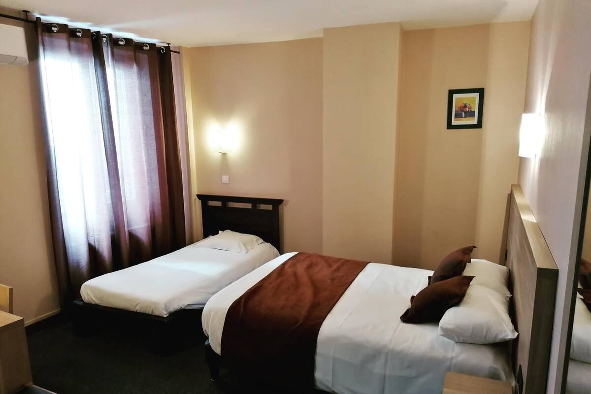 A hotel room with two single beds, a desk, and a chair.