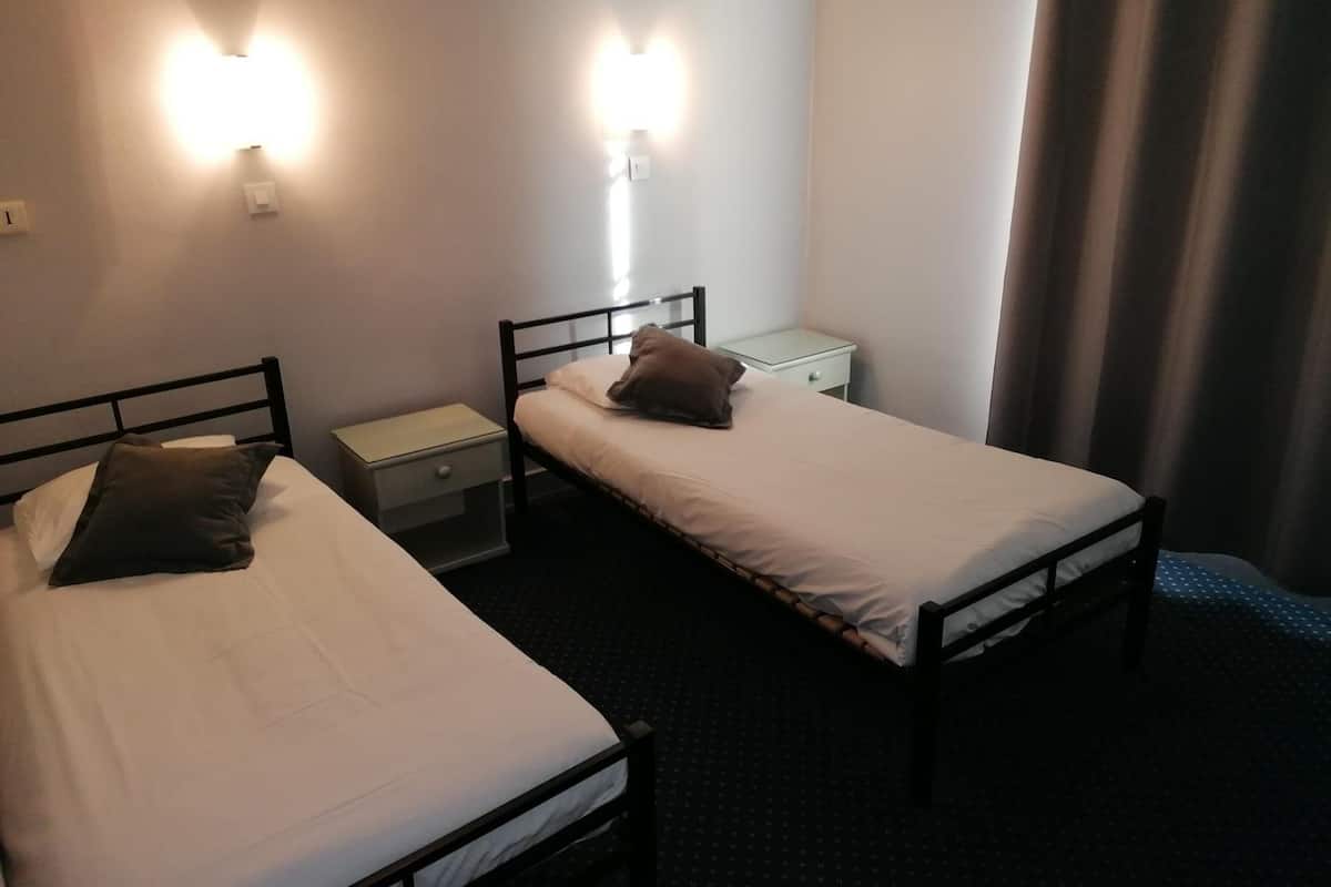A hotel room with two single beds, a small bedside table with a lamp, and a nightstand.