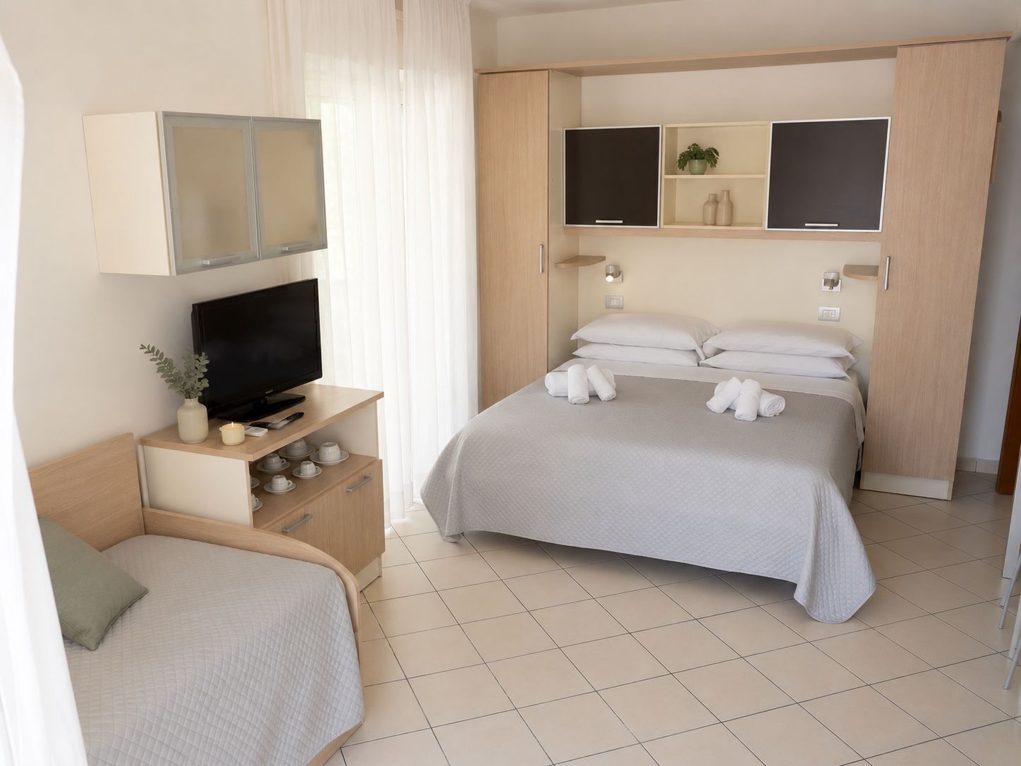 A hotel room with a bed, a TV, a desk with a computer, and a small cabinet.
