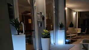 Un vestíbulo de hotel con suelo de baldosas, grandes macetas, un mostrador de recepción y una zona de estar con sillones.