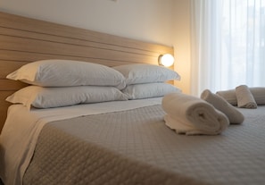 A neatly made bed with white linens and pillows, a wooden headboard, and a bedside lamp.