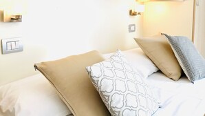 Habitación de hotel con cama, almohadas, televisión montada en la pared, estante con plantas y un enchufe.