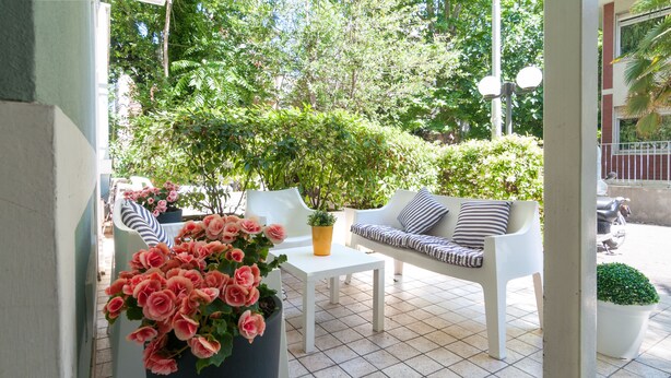Un espace patio aménagé avec un canapé blanc, une petite table et un pot de fleurs orné de fleurs roses.