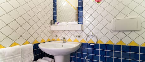 Ein Badezimmer mit einem weißen Waschbecken, Spiegel und Toilette. Handtücher liegen auf dem Boden gestapelt.