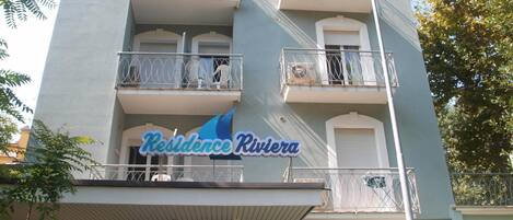 A multi-story building with balconies, a sign reading "Residence Riviera," and a covered entrance area.