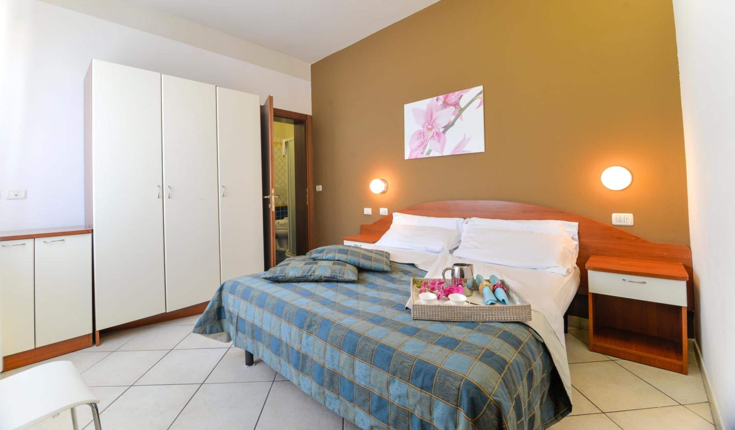 Un dormitorio con cama, mesitas de noche, un armario y un baño visible a través de una puerta abierta.