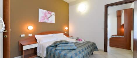 A bedroom with a bed, bedside tables, a nightstand, a wall-mounted light, a mirror, and a door.
