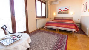 A bedroom with a bed, a radiator, a window with curtains, a ceiling fan, and a painting on the wall. - Budavar Bed and Breakfast (Budapest)