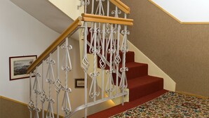 A staircase with ornate white metal railings and wooden handrails, carpeted steps, and a framed picture on the wall. - Budavar Bed and Breakfast (Budapest)
