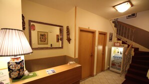 A reception area with a wooden desk, a mirror, a refrigerator, and a staircase. - Budavar Bed and Breakfast (Budapest)