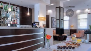A hotel lobby with a bar area, a dining table with breakfast items, and a decorative vase with a flower. - B&B Hotels Park Hotel Mondovi (Mondovi)