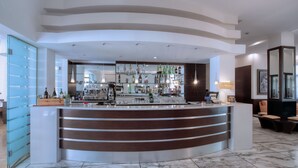 A modern bar area with a curved counter, shelves with bottles, and a seating area with cushioned chairs. - B&B Hotels Park Hotel Mondovi (Mondovi)